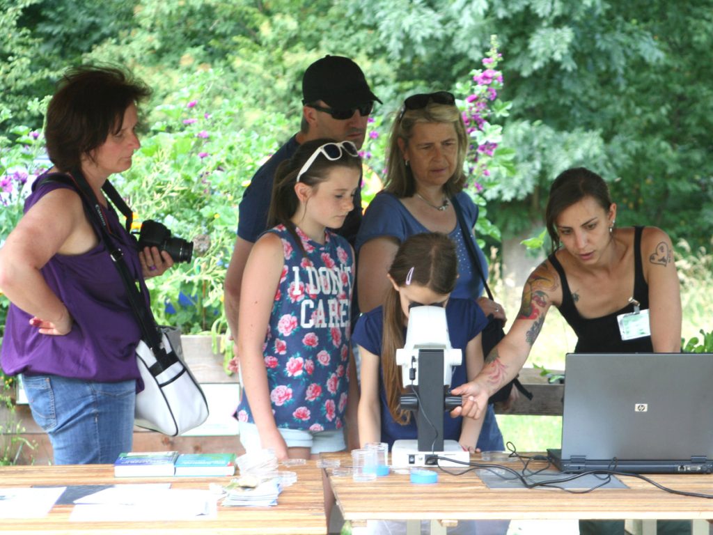 Mitarbeiterin erklärt Besucher:innen das Mikroskop